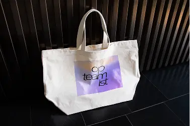 Totebag de lona blanca con el wordmark de Opteamist sobre un recuadro en degradado morado
